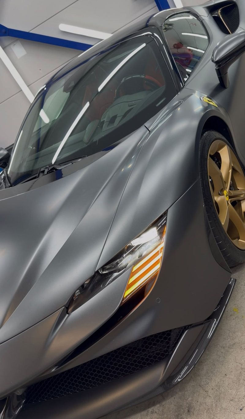 Voorzijde van een matgrijze Ferrari SF90 Spider met brandende koplamp en gouden velg na detailing bij JS Detail Studio in IJmuiden